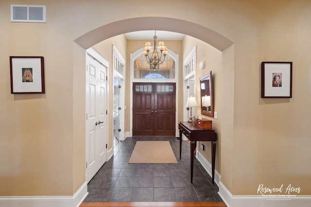 entrance foyer featuring baseboards, visible vents, a chandelier, and arched walkways