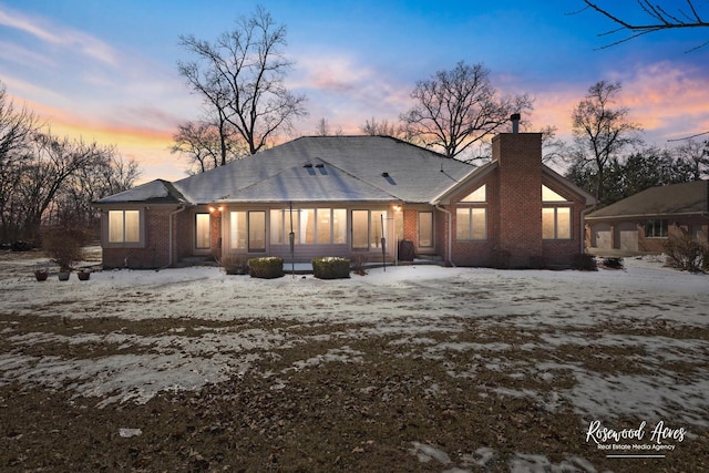 snow covered house featuring brick siding and a chimney