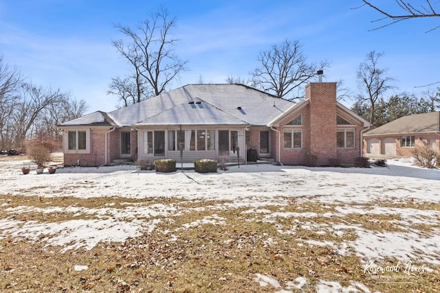 snow covered back of property with entry steps, brick siding, and a chimney