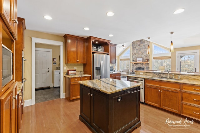 kitchen featuring a kitchen island, brown cabinets, hanging light fixtures, stainless steel appliances, and a sink