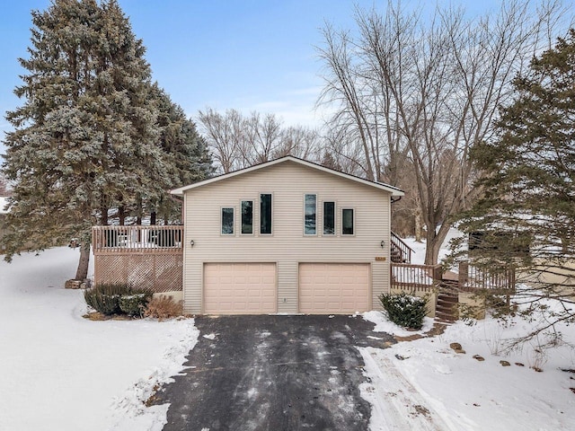 view of snow covered exterior with an attached garage, driveway, a wooden deck, and stairs