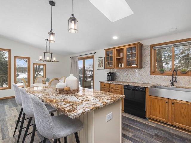 kitchen with brown cabinets, hanging light fixtures, a sink, vaulted ceiling with skylight, and dishwasher