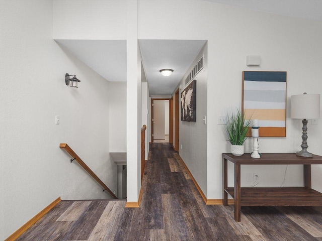 hall featuring dark wood-style floors, baseboards, visible vents, and an upstairs landing