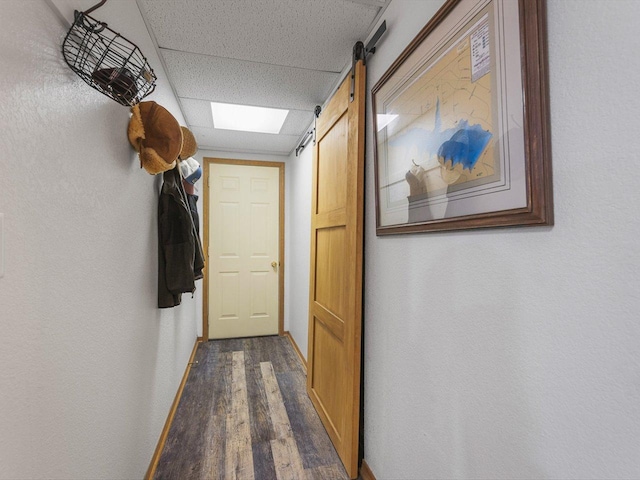 corridor featuring dark wood-type flooring, a paneled ceiling, baseboards, and a barn door