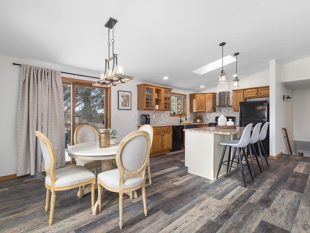 dining room with vaulted ceiling with skylight, dark wood-type flooring, and baseboards