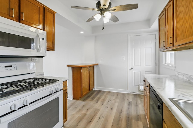 kitchen featuring brown cabinetry, white appliances, a sink, and light wood-style flooring