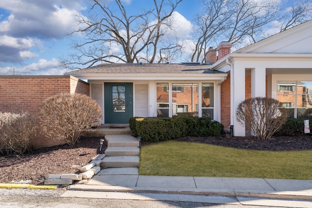 doorway to property with a yard, brick siding, and a chimney