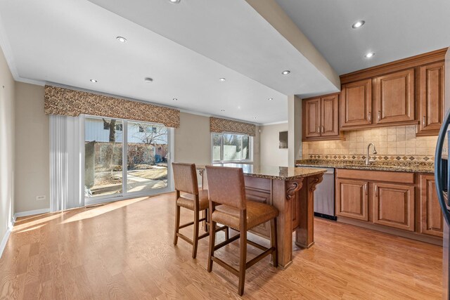 kitchen with light wood finished floors, a center island, ornamental molding, brown cabinetry, and stainless steel dishwasher