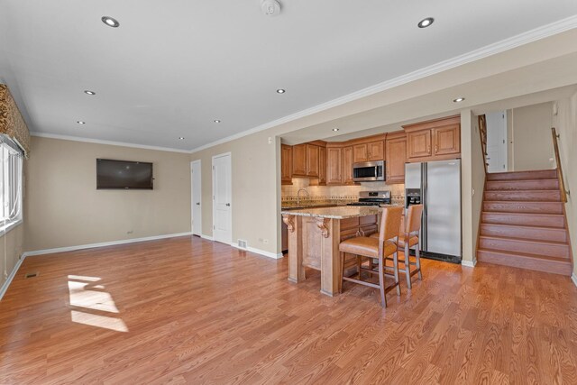 kitchen with ornamental molding, stainless steel appliances, a kitchen bar, light wood-type flooring, and a center island