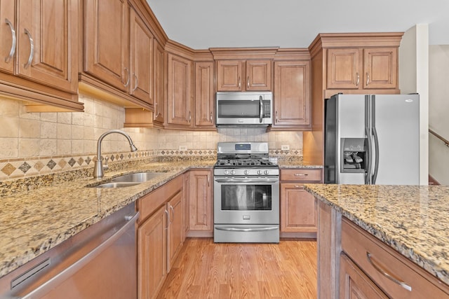 kitchen featuring light stone counters, light wood-style flooring, appliances with stainless steel finishes, and a sink