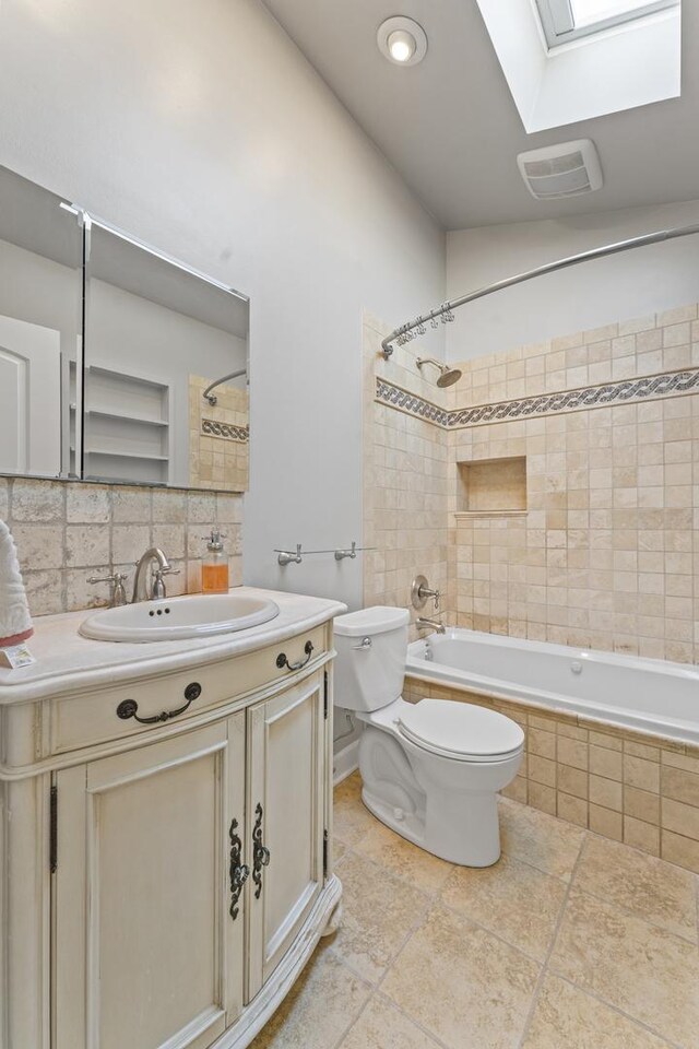 full bathroom featuring visible vents, toilet, a skylight, tiled shower / bath combo, and vanity