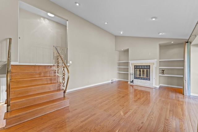 unfurnished living room with built in shelves, baseboards, a tiled fireplace, stairs, and wood finished floors