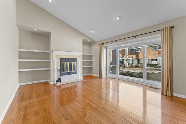 unfurnished living room featuring vaulted ceiling, built in features, light wood-style floors, and a tile fireplace