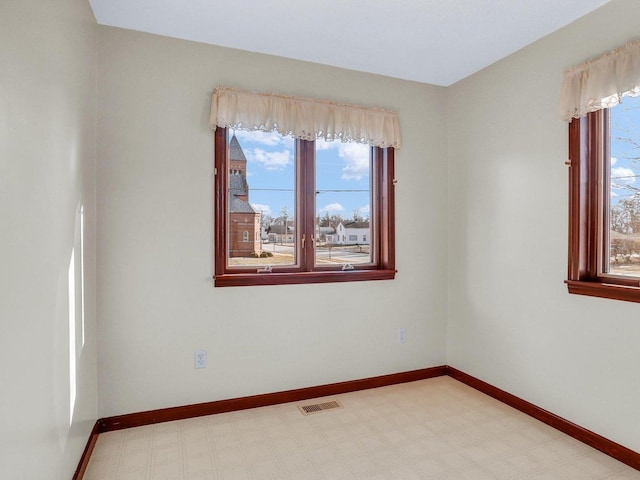 empty room with light floors, visible vents, and baseboards