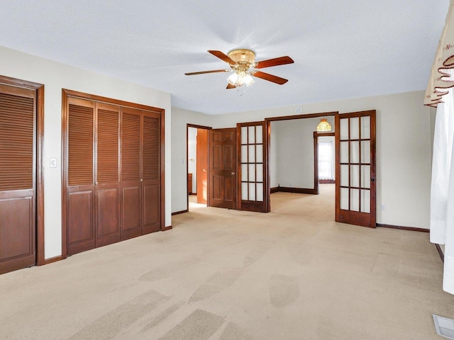 unfurnished bedroom with multiple closets, french doors, light colored carpet, and baseboards