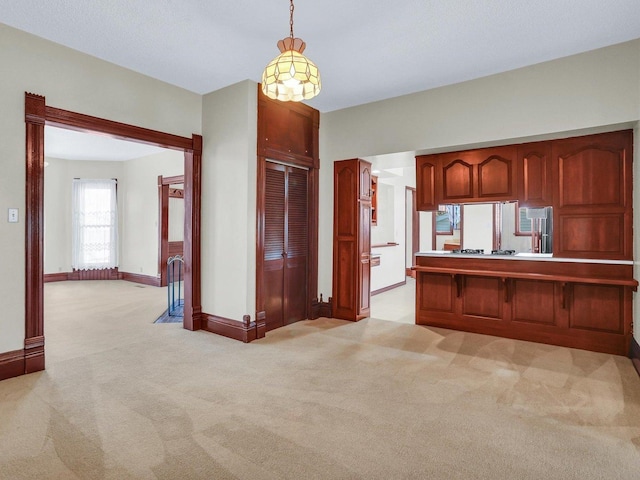 kitchen with reddish brown cabinets, pendant lighting, gas stovetop, light colored carpet, and baseboards