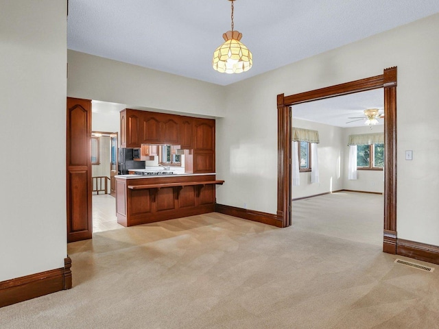 kitchen with light carpet, visible vents, brown cabinets, open floor plan, and hanging light fixtures