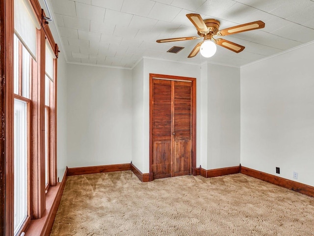 empty room with light carpet, baseboards, visible vents, a ceiling fan, and ornamental molding