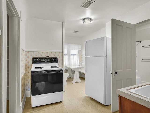 kitchen with electric stove, light countertops, visible vents, freestanding refrigerator, and a sink