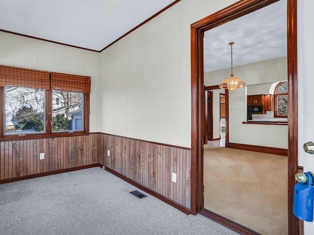 spare room featuring a wainscoted wall, crown molding, visible vents, light carpet, and wooden walls