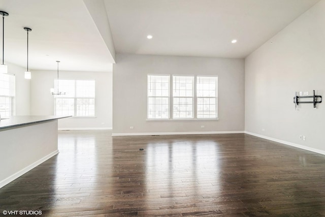 unfurnished living room with dark wood finished floors, an inviting chandelier, recessed lighting, and baseboards