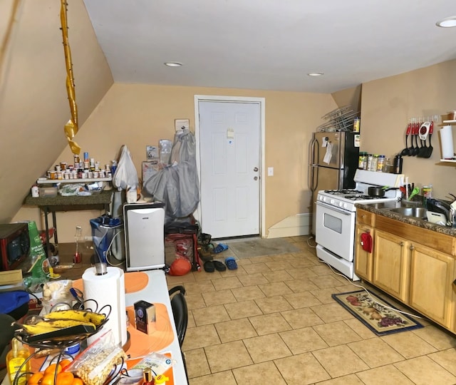 kitchen with dark countertops, white gas range, a sink, and freestanding refrigerator