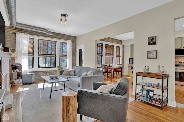 living room featuring baseboards, light wood finished floors, and brick wall