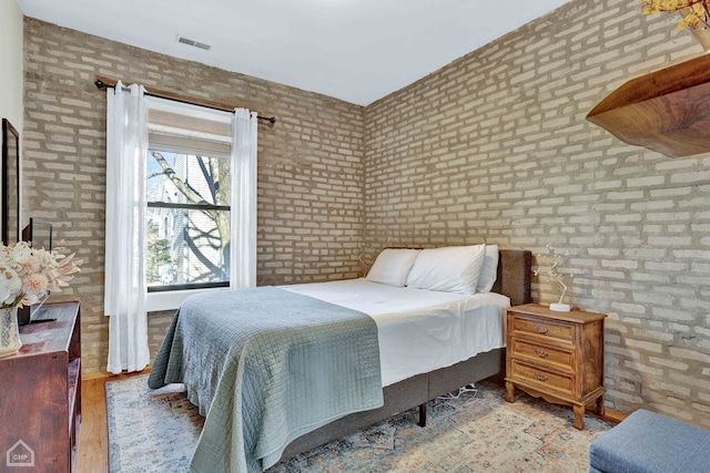 bedroom with visible vents, light wood-style flooring, and brick wall