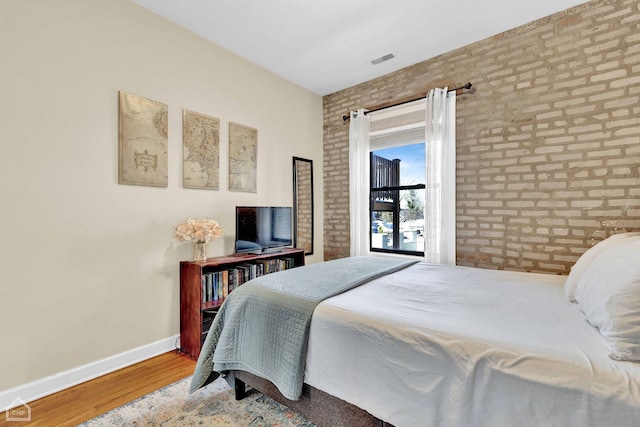 bedroom featuring brick wall, wood finished floors, visible vents, and baseboards