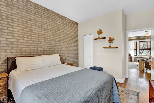 bedroom featuring brick wall, baseboards, and wood finished floors