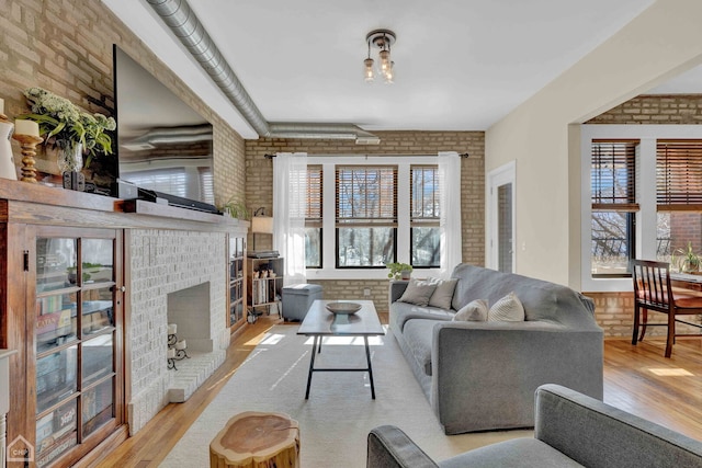 living room with brick wall, a brick fireplace, and light wood-style floors