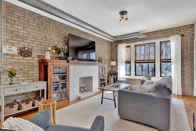 living area featuring light wood-style floors, brick wall, and a fireplace