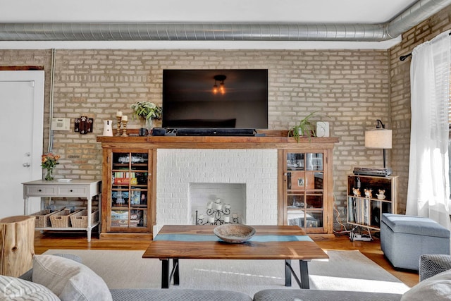 living area featuring a fireplace, brick wall, and wood finished floors