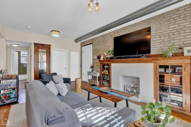 living area with brick wall, a fireplace, and wood finished floors