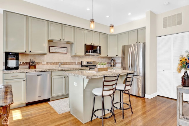 kitchen featuring stainless steel appliances, visible vents, hanging light fixtures, a kitchen island, and a sink