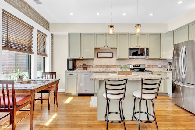 kitchen featuring light stone counters, a center island, hanging light fixtures, stainless steel appliances, and light wood-style floors