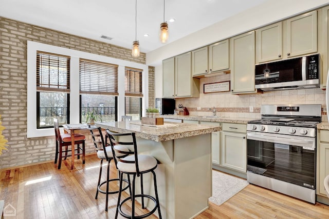 kitchen with light wood finished floors, stainless steel appliances, visible vents, hanging light fixtures, and a kitchen island