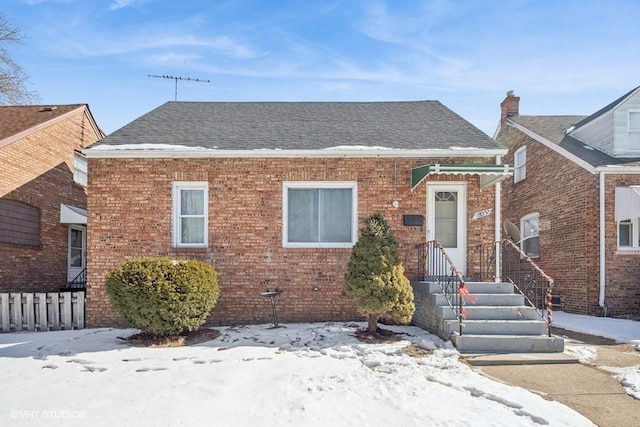 view of front of property featuring brick siding, a shingled roof, and fence