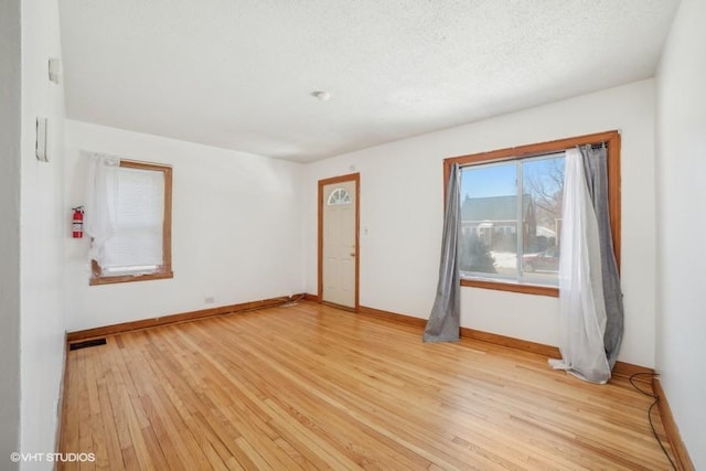 spare room featuring light wood-style floors, baseboards, visible vents, and a textured ceiling