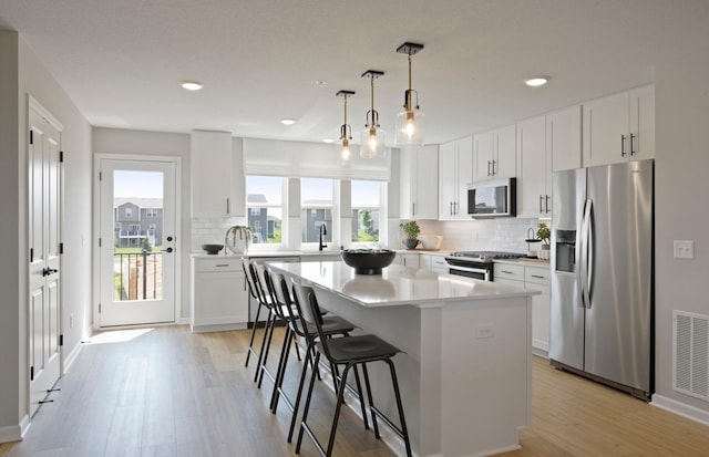 kitchen with white cabinetry, light countertops, appliances with stainless steel finishes, a center island, and decorative light fixtures