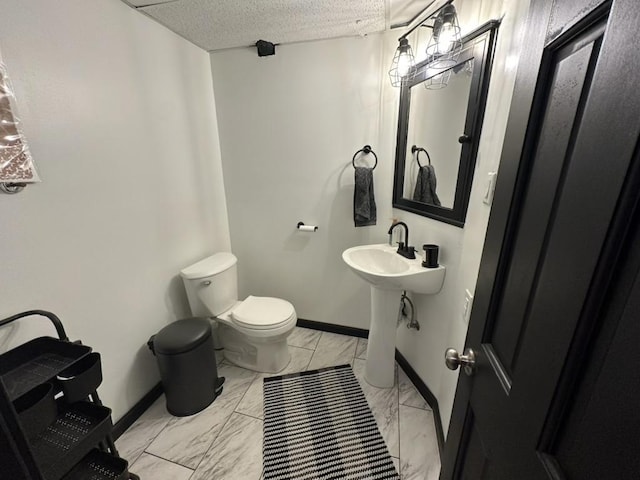 half bathroom with a textured ceiling, marble finish floor, toilet, and baseboards