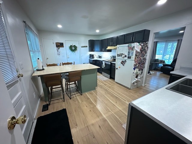 kitchen with electric range, a kitchen breakfast bar, dark cabinets, freestanding refrigerator, and light countertops