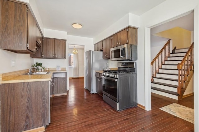 kitchen with appliances with stainless steel finishes, light countertops, a sink, and dark wood-type flooring