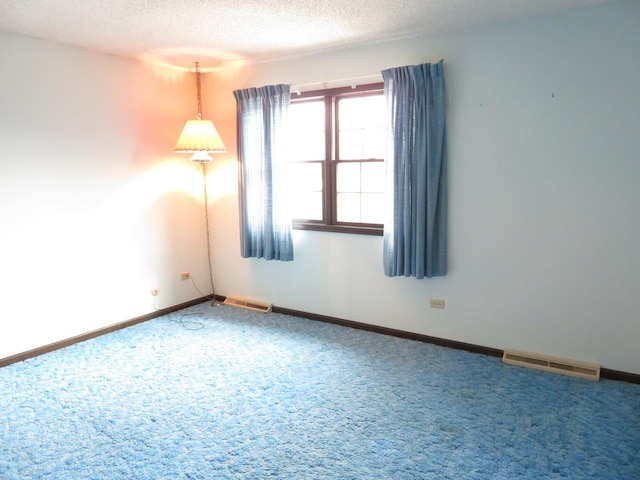 unfurnished room with a textured ceiling, carpet flooring, visible vents, and baseboards