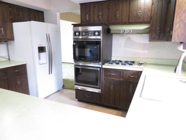 kitchen with under cabinet range hood, white appliances, a sink, light countertops, and dark brown cabinets