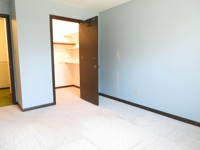 unfurnished bedroom with light carpet, baseboards, a walk in closet, and a closet