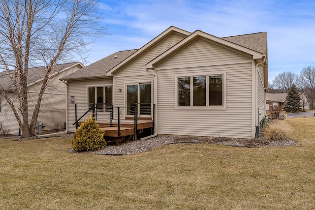 rear view of property featuring a deck, roof with shingles, and a lawn