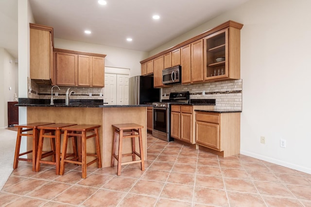 kitchen featuring a breakfast bar, dark stone countertops, a peninsula, stainless steel appliances, and light tile patterned flooring