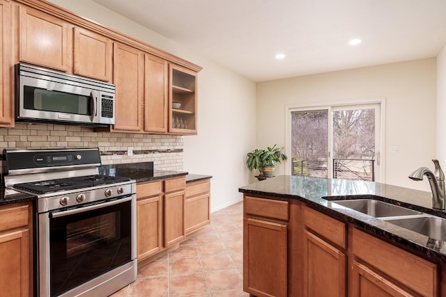 kitchen featuring stainless steel appliances, dark stone counters, a sink, and decorative backsplash