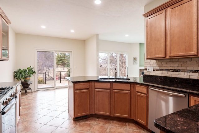 kitchen with a peninsula, a sink, appliances with stainless steel finishes, decorative backsplash, and dark stone counters